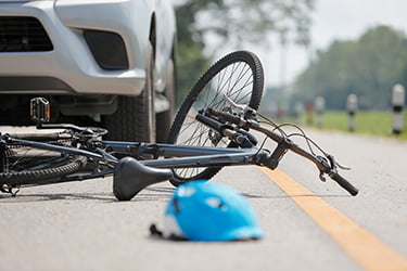 Bike and helmut laying on the ground in front of a car after an accident