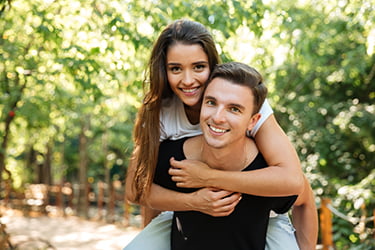 Young man giving a young woman a piggyback ride with trees in the background