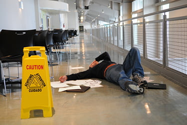 Man laying on his back on the floor wiht his hand over his face next to a yello Caution sign for a Premises Liability case